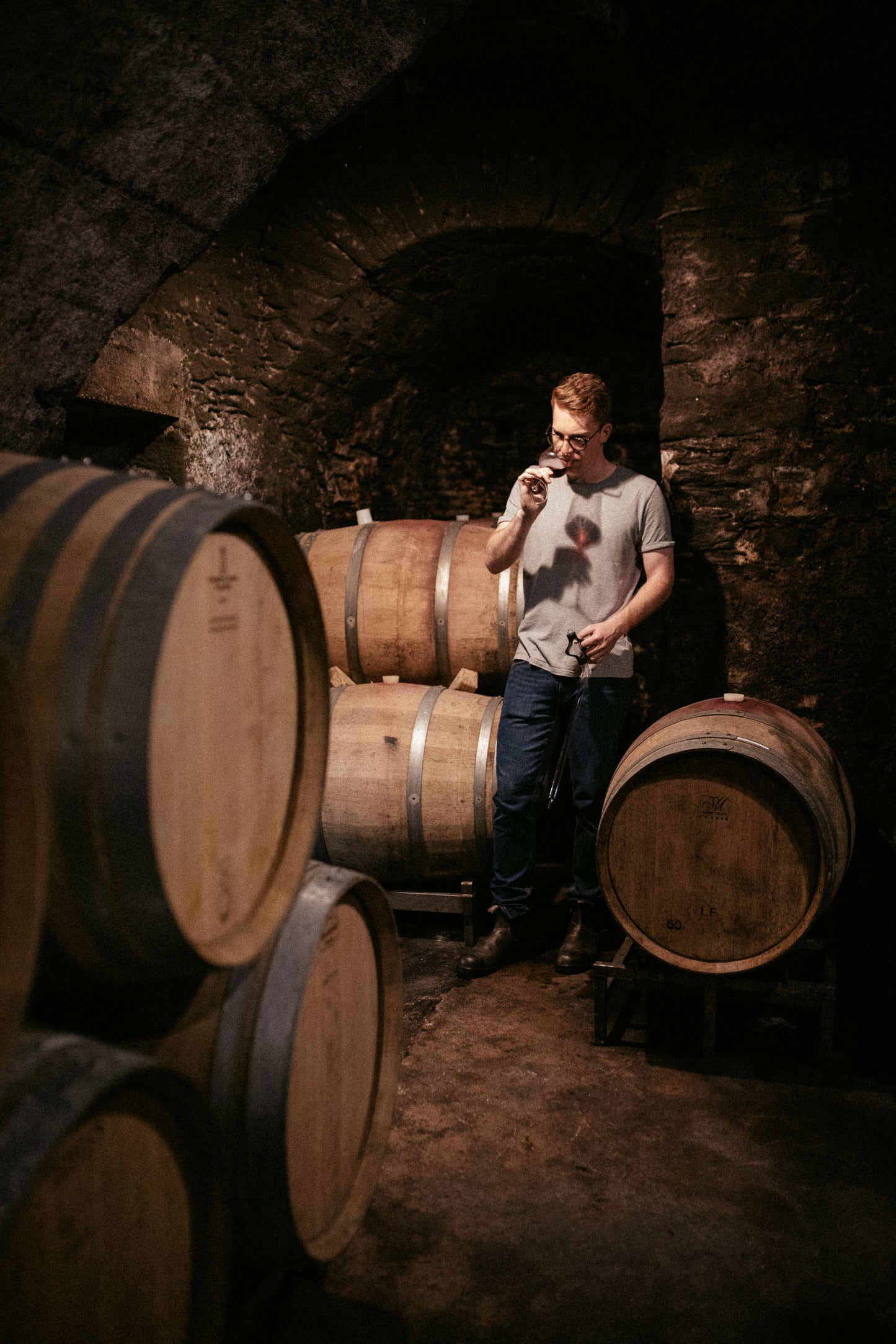
                  
                    Daniel Fries im Rotweinkeller beim Wein probieren, umgeben von Weinfässern. 
                  
                